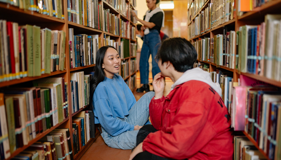 dos jóvenes conversando en una biblioteca