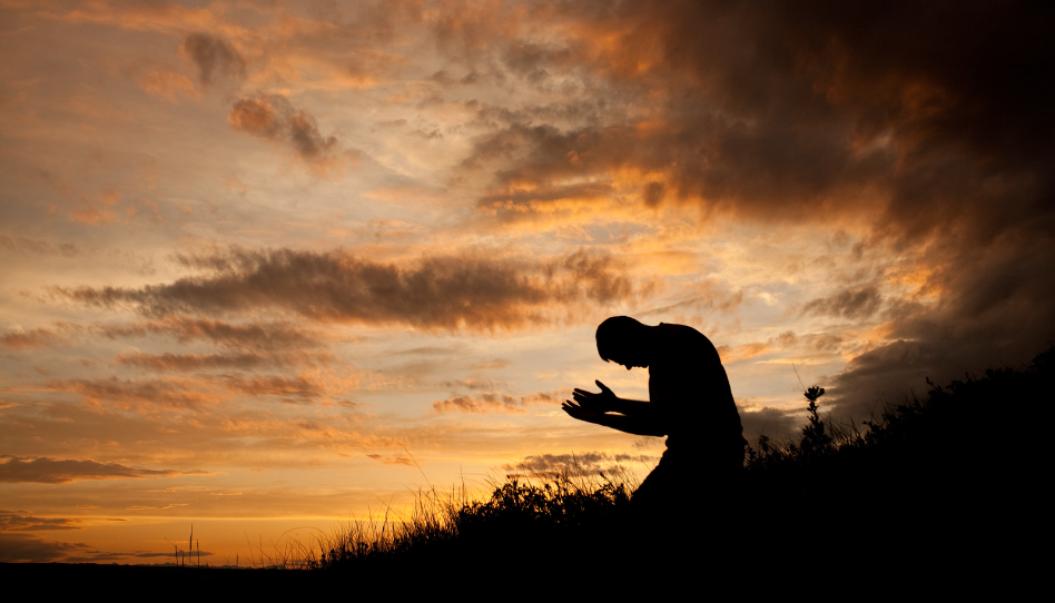 hombre de rodillas orando con las manos extendidas en un atardecer
