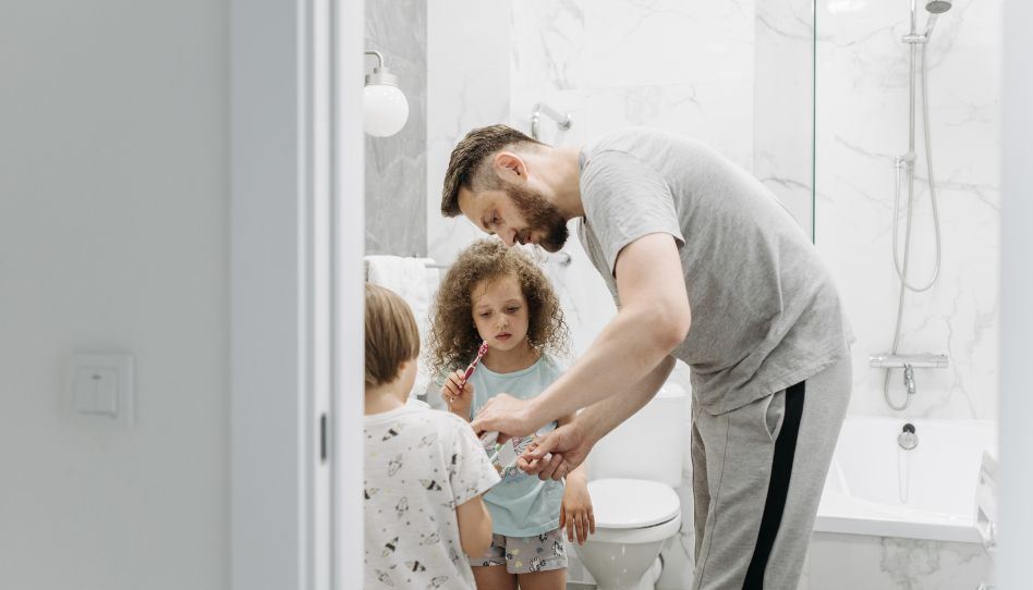 papá ayudando a sus hijas a cepillarse los dientes 