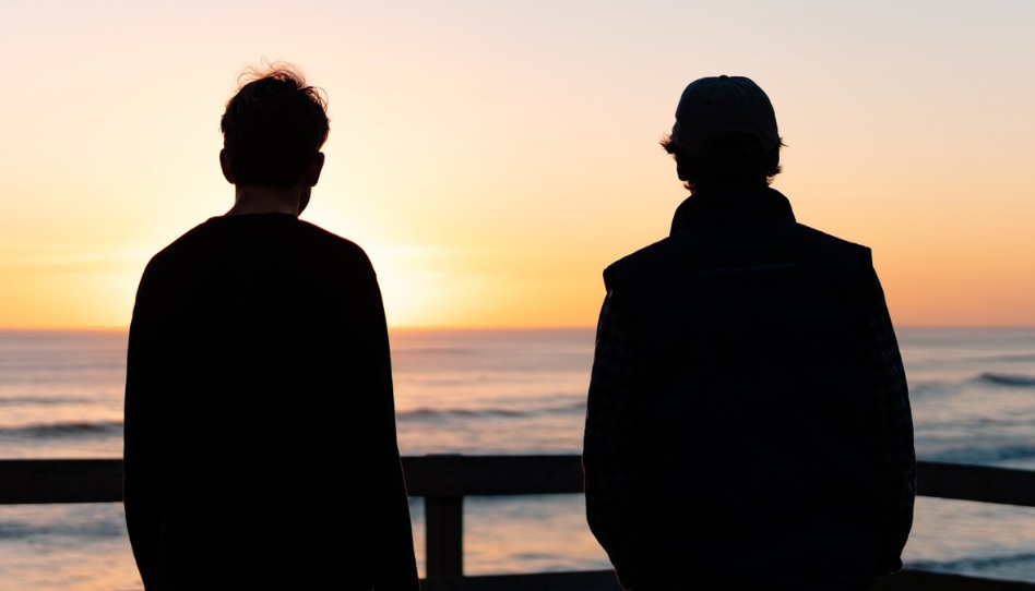 dos hombre mirando al mar en un atardecer
